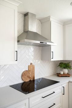 a kitchen with white cabinets and black counter tops, an oven hood and cutting board