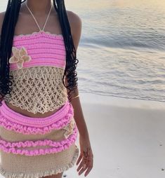 a woman standing on top of a beach next to the ocean wearing a crocheted dress