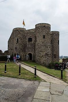 an old stone castle with flags on top and people walking around the gated area