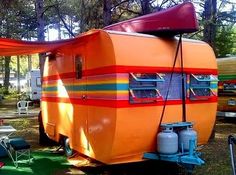 an orange trailer parked in the grass next to other trailers and camping equipment with trees in the background