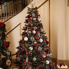 a decorated christmas tree with red, white and blue ornaments on it in front of a staircase