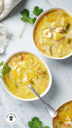 two bowls filled with soup on top of a white counter next to cilantro and parsley