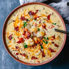 a bowl of potato soup with bacon, cheese and green onions in it on a blue surface