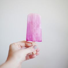 a hand holding a popsicle with pink ice cream on it's tip, against a white background