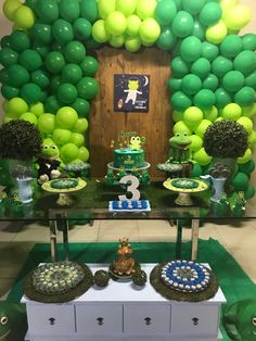 a table topped with lots of green and white balloons next to a wall covered in balloons