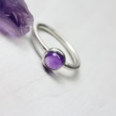 February's birthstone amethyst is such a popular color. This gorgeous deep dark orchid purple warms my heart. I decided to set this 6mm cabochon in a simple modern setting. A stackable silver ring with a trendy colored round gemstone dot in a circular bezel. Ring shank measures 1.9mm. **Made to order in your size (please allow 3-5 days) nangijalajewelry.etsy.com *Gemstone colors might vary slightly Amethyst Ring With Natural Stones For Healing, Spiritual Purple Cabochon Jewelry, Purple Sterling Silver Birthstone Ring As Gift, Purple Sterling Silver Birthstone Ring For Gift, Anniversary Amethyst Cabochon Gemstone, Amethyst Cabochon Gemstones For Anniversary, Anniversary Cabochon Amethyst Gemstone, Cabochon Amethyst Gemstones For Anniversary, Oval Purple Amethyst Ring With Natural Stones