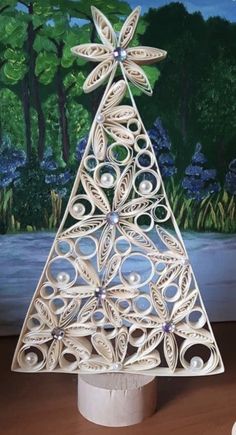 a christmas tree made out of paper on top of a wooden table next to a painting