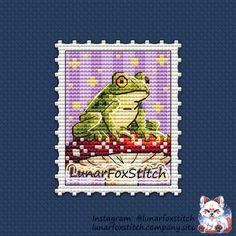 a cross stitch frog sitting on top of a piece of fabric