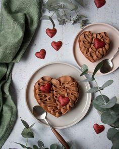 two heart shaped cakes sitting on top of plates next to leaves and flowers with spoons