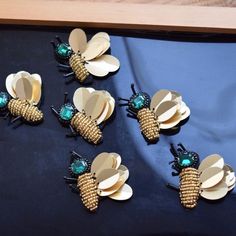 six gold and green bee brooches on a black table top with blue fabric