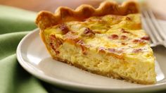 a piece of quiche on a white plate with a fork and green table cloth