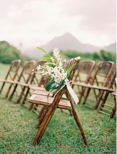 an arrangement of wooden folding chairs with flowers tied to the back are set up for a wedding ceremony