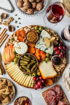 an assortment of cheeses, meats and nuts on a platter surrounded by wine glasses