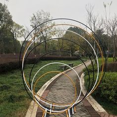 a metal sculpture sitting on top of a brick walkway next to a lush green park