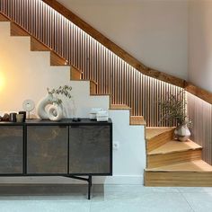 a wooden stair case next to a table with vases on it and a lamp in the background