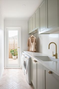 A beautiful pastel sage green laundry features brushed brass tapware. A washing machine is neatly stored under the bench. Sage Laundry, Laundry Cabinet, Abi Interiors, Laundry Room Tile, Green Laundry, Three Birds Renovations, Laundry Design, Modern Laundry Rooms, Three Birds