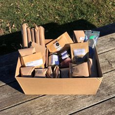 an open cardboard box filled with food sitting on top of a wooden table next to grass