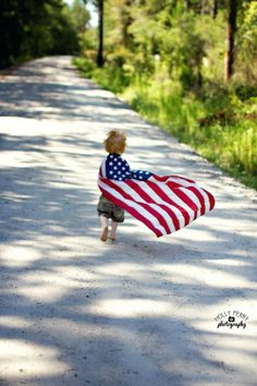 a little boy holding an american flag on the road