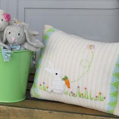 two stuffed animals sitting on top of a pillow next to a green bucket with a bunny in it