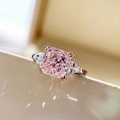 a pink diamond ring sitting on top of a white surface with sunlight coming through the window