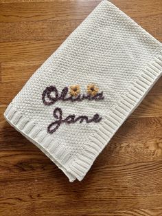 a white knitted dish towel with embroidered words and flowers on the front that says, ohana jane