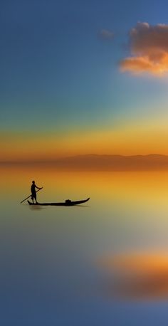 a man riding on top of a boat in the ocean at sunset with clouds above