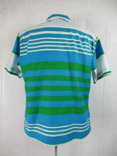 "Vintage 1960s short sleeve Rockabilly shirt. Made of green, blue and white striped cotton. Has a button front, straight hem and matching pattern pocket. Made by Bronzini. Size medium. Actual measurements are 45\" at the chest 43\" at the waist 17.5\" shoulder seam to shoulder seam 27\" overall length In excellent unused condition. New old stock." Blue Collared Shirt With Vertical Stripes, Green Shirt With Striped Collar For Summer, Green Cotton Shirt With Striped Collar, Green Vertical Striped Shirt For Summer, Green Vertical Striped Summer Shirt, Green Button-up Shirt With Striped Collar, Green Vertical Stripes Button-up Shirt, Retro Short Sleeve Shirt, Retro Green Short Sleeve Shirt For Summer