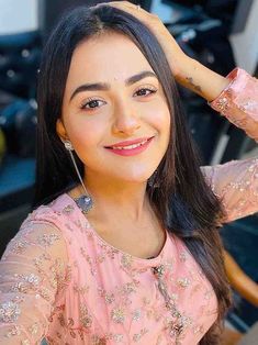 a woman with long black hair wearing a pink dress and smiling at the camera while sitting in a chair