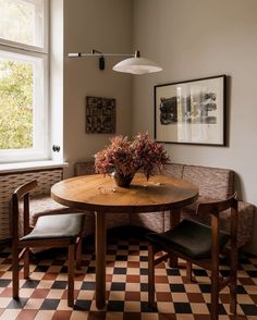 a wooden table sitting under a window next to two chairs and a vase with flowers on it