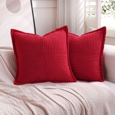 two red pillows sitting on top of a white couch