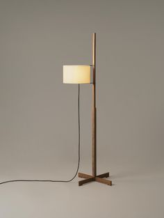 a floor lamp with a wooden base and a white shade on the light bulb is plugged in