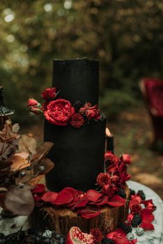 a black and red wedding cake with flowers on the top is surrounded by greenery