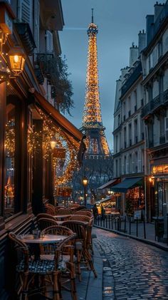 the eiffel tower in paris is lit up at night, with tables and chairs outside