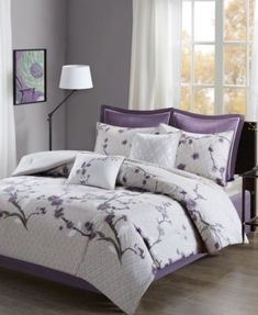 a bed with purple and white comforters in a room next to a lamp on a table