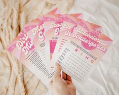 a person holding five pink flyers on top of a bed