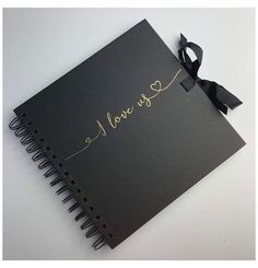 a black spiral notebook with gold foil writing on the cover and a ribbon tied around it