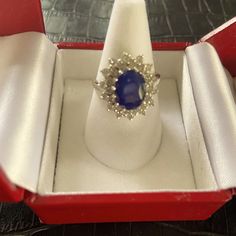 an open red box with a blue stone ring in it's center, on top of a table