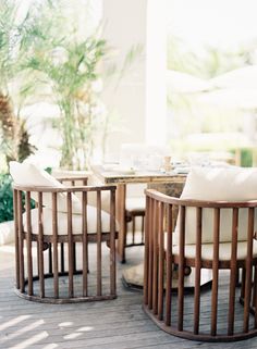 there are chairs and tables on the wooden deck near each other with white cushiones