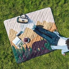 a woman laying on the grass with her feet up in front of a picnic blanket