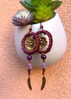 These earrings are ready for an adventure, large or small. The hoops are different hues of red, and are filled with a golden-colored Poppy charm. Hanging from the hoop are a purple Lepidolite, small Garnet, a lavender glass bell, and swinging at the bottom is a metal Feather charm. The earrings were hand beaded with no wire. They are lightweight, have some flexibility yet retain their shape. Measurements: length 3 3/4 inches; 1 1/4 inch across the hoop. One of a kind set. Handbeaded with love in New Mexico. Bohemian Purple Hoop Earrings With Round Beads, Purple Bohemian Hoop Earrings, Bohemian Red Hoop Earrings With Colorful Beads, Bohemian Purple Round Hoop Earrings, Purple Bohemian Round Hoop Earrings, Red Hoop Earrings For Festival, Red Bohemian Adjustable Hoop Earrings, Adjustable Red Bohemian Hoop Earrings, Red Adjustable Bohemian Hoop Earrings