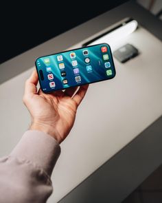 a person holding an iphone in their hand with other devices on the table behind them