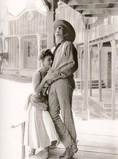 an old black and white photo of a man standing next to a woman on a porch