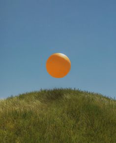 an orange frisbee flying in the air over a grassy hill under a blue sky