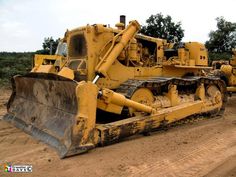 two large yellow bulldozers sitting on top of a dirt road