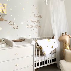 a baby's room decorated in white and gold with stars on the wall, crib bedding, rocking chair and dresser