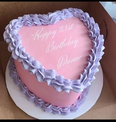 a pink heart shaped cake with purple ruffles on it's side in a box