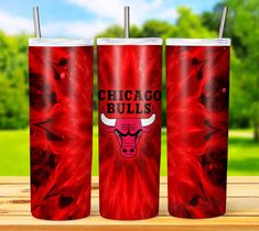 three red chicago bulls tumblers sitting on top of a wooden table with trees in the background