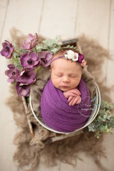 a newborn baby wrapped in purple sits in a basket with flowers