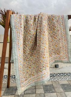 a blanket is hanging on a wooden stand outside in front of a tiled floor and palm tree