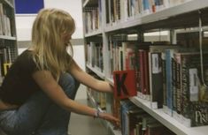 a woman picking up a book from a shelf in a library